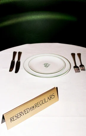 A restaurant table with a white tablecloth, plate, and a gold sign reading 