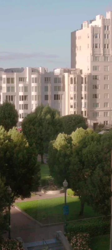 A view from a hotel window looks out over the green trees of Huntington Park and the white buildings of Nob Hill.