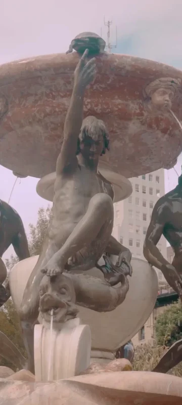 The ornate bronze Fountain of the Tortoises in Huntington Park, with statues of mermen and city buildings in the background.