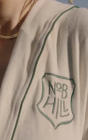 Close-up of a white spa robe with green piping and the embroidered 