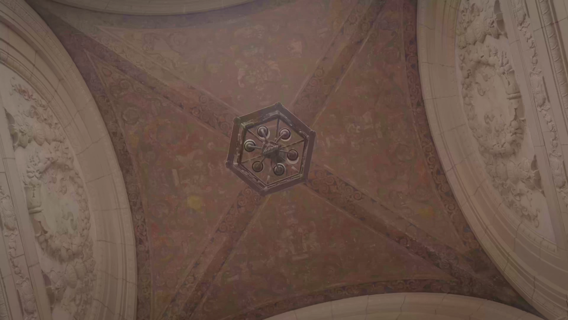 A view looking straight up at an ornate, painted, vaulted ceiling with a central, antique light fixture.