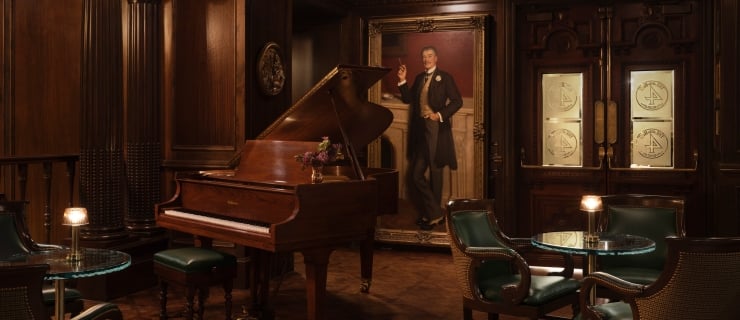 A dimly lit, upscale lounge featuring dark wood paneled walls, intricate parquet flooring, and classic architecture with fluted columns