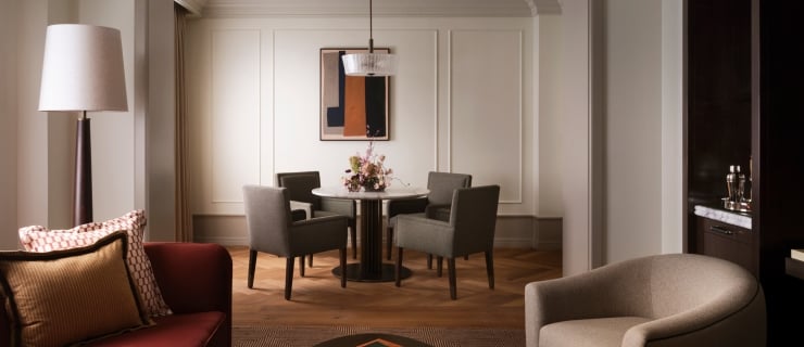 A warm, elegantly designed living and dining suite features a rich reddish-brown sofa with decorative throw pillows in the left foreground