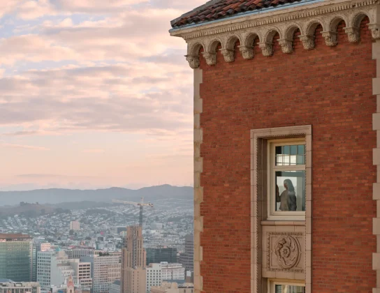 Exterior view of The Huntington Hotel; a woman peers through a window on the top floor, overlooking San Francisco