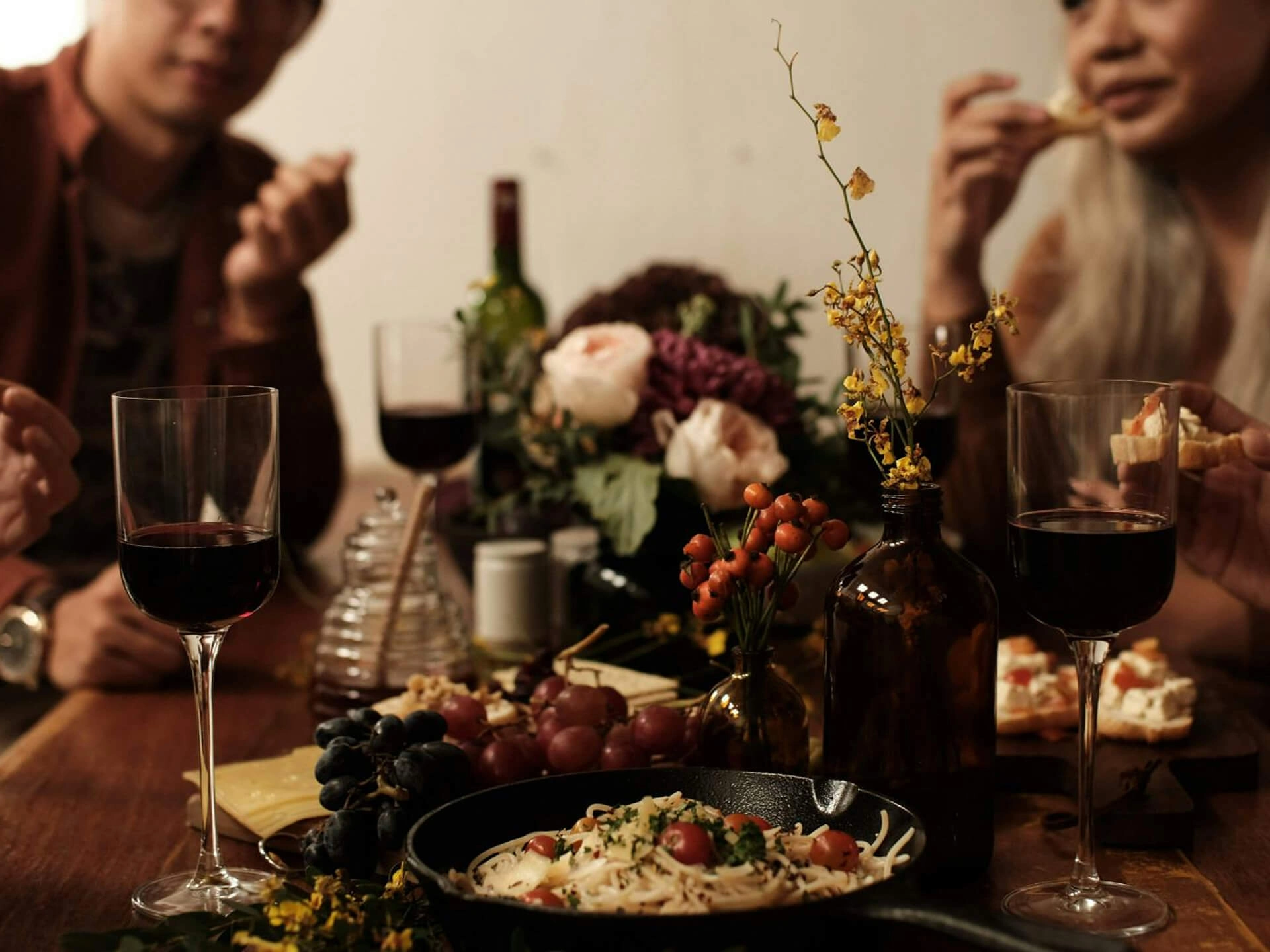 Close-up of a dinner table with wine, pasta, and flowers during a social gathering