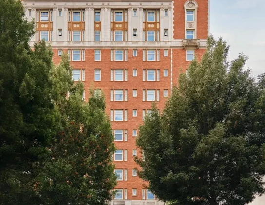 Exterior view of a grand red brick historic building framed by lush green trees