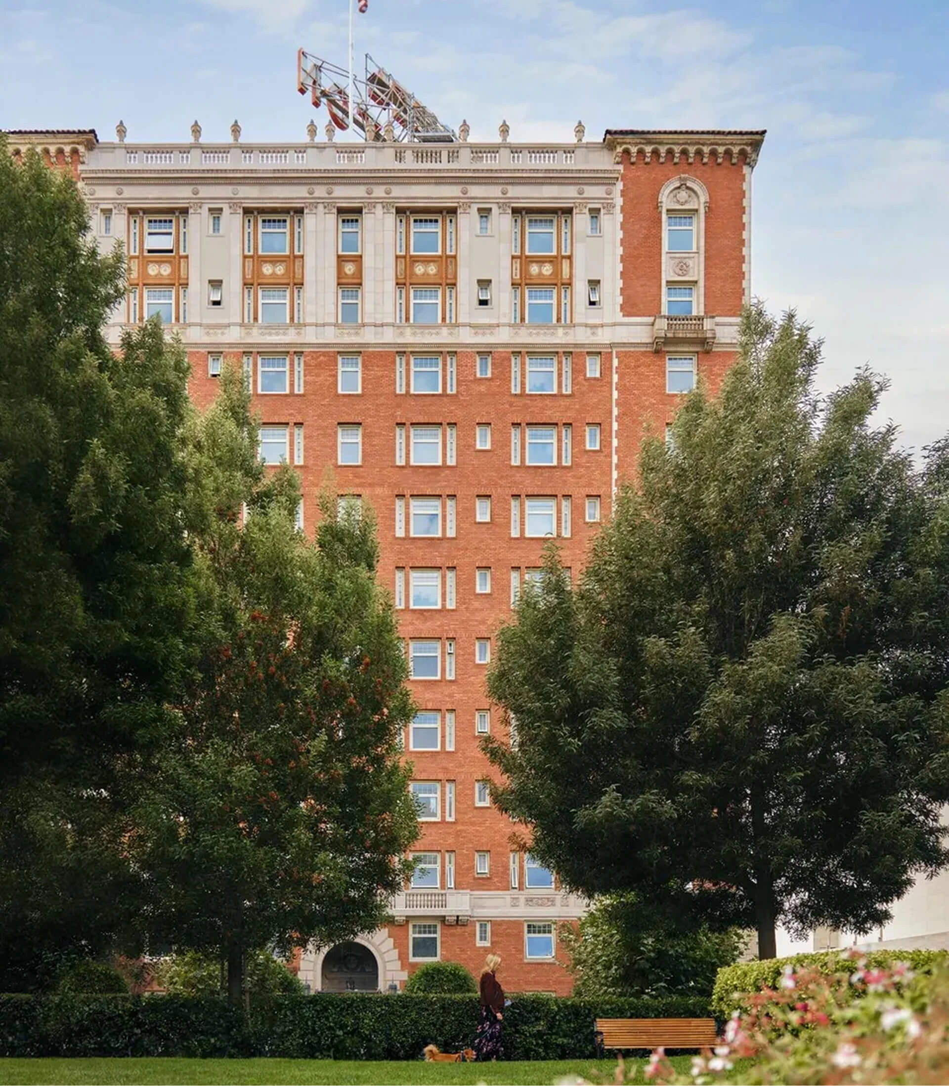 Exterior view of a grand red brick historic building framed by lush green trees