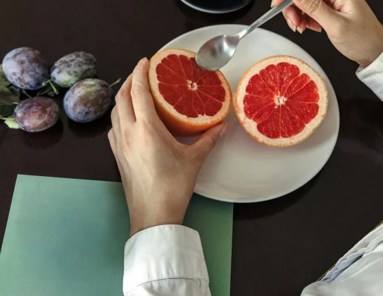 A fresh grapefruit halved on a white plate with a cup of coffee