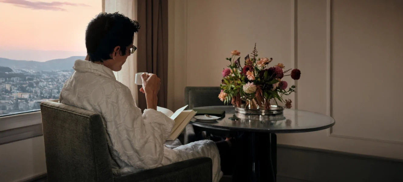 A man in a white robe reads a book while enjoying his coffee