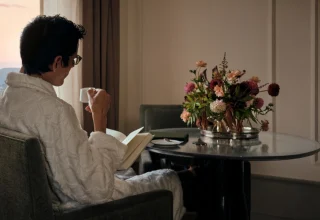 A man in a white robe reads a book while enjoying his coffee