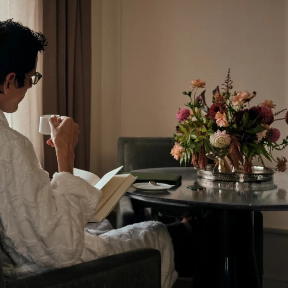A man in a white robe reads a book while enjoying his coffee