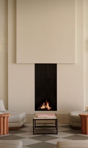 A plaster fireplace with two large lounge seats and a coffee table in a sunny atrium.
