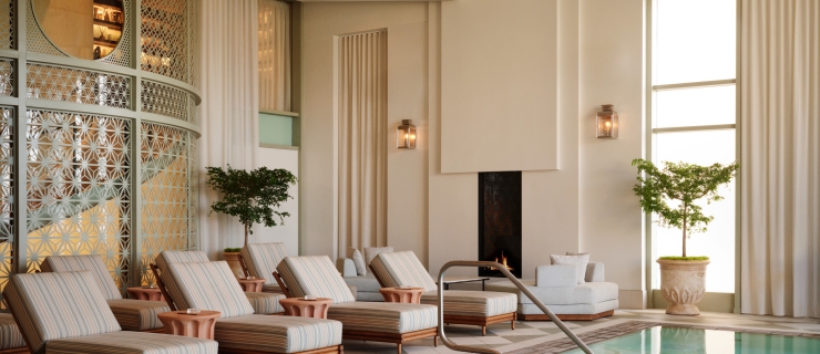 An indoor luxury swimming pool area with a row of cushioned chaise lounges lined up along the water's edge