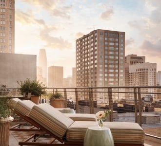 Three sun loungers on a patterned outdoor rug on a terrace overlooking San Francisco