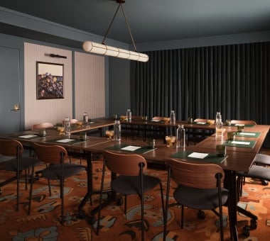A professionally styled conference room features dark slate-blue walls and a matching ceiling, with a large square shaped wooden meeting table