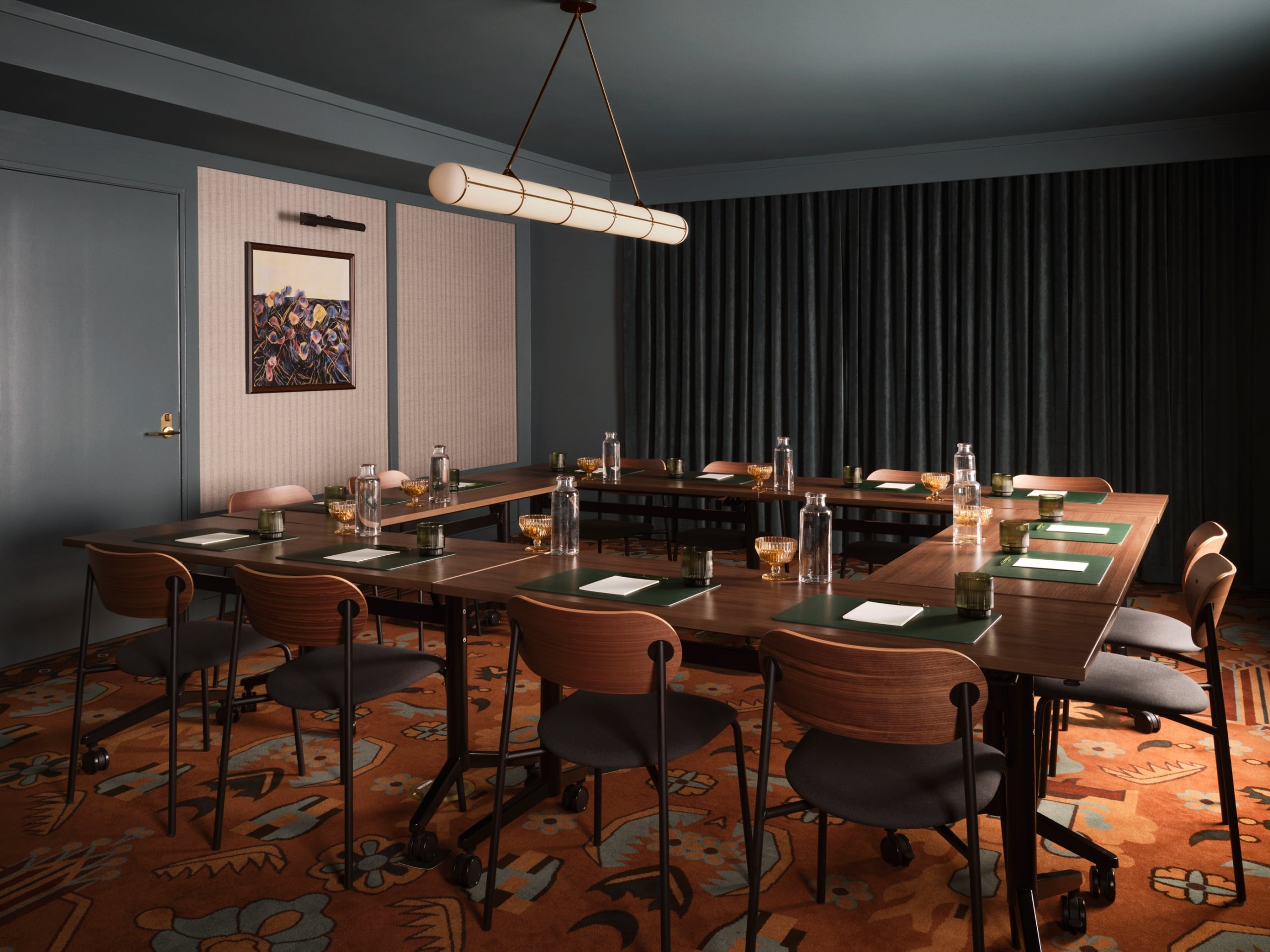 A professionally styled conference room features dark slate-blue walls and a matching ceiling, with a large square shaped wooden meeting table