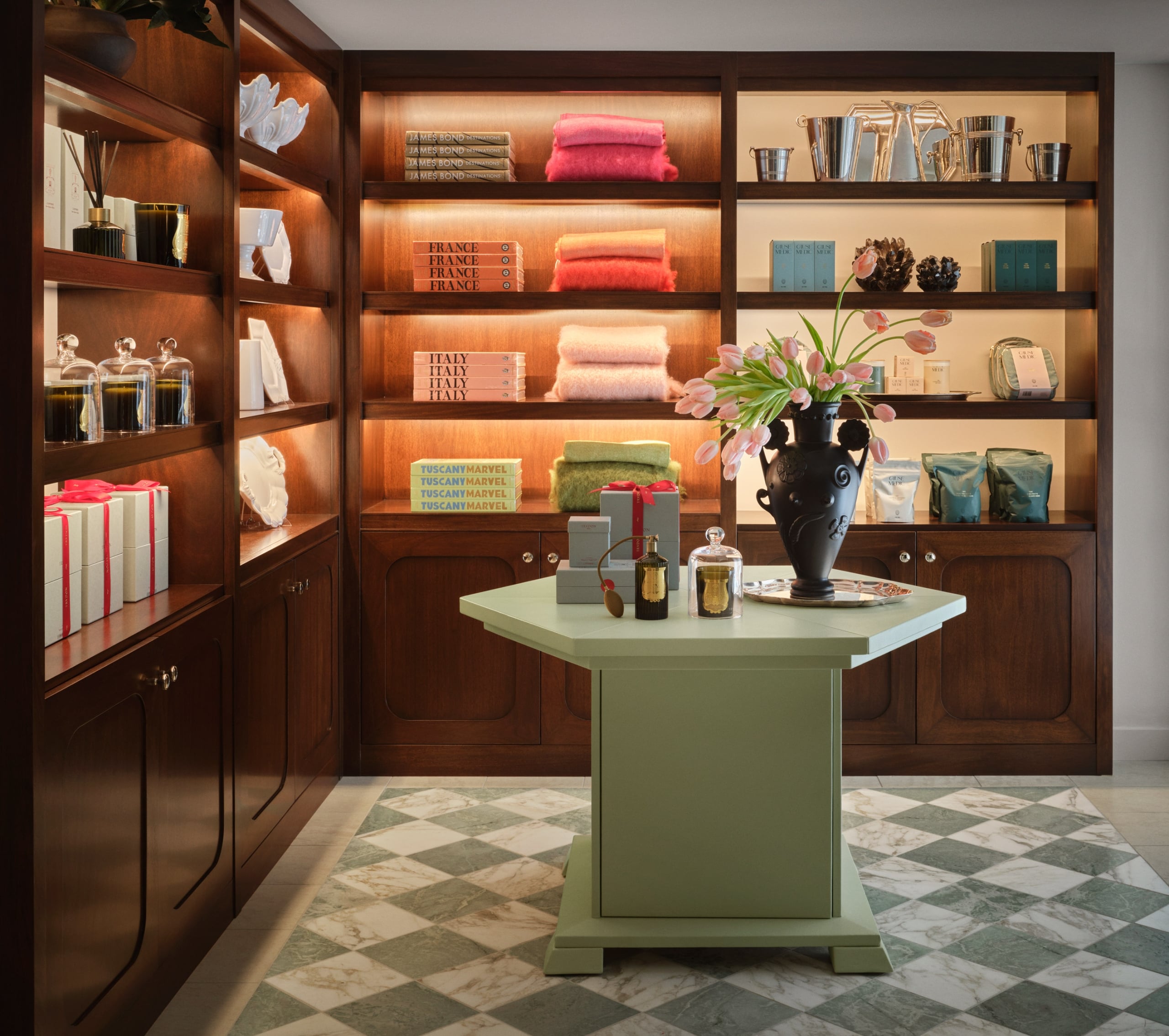 A well-lit luxury boutique display features built-in dark wood shelving filled with neatly stacked textiles, books, and decorative items