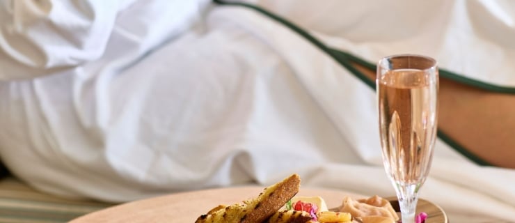 A woman lounging in a white spa robe with green trim enjoys a charcuterie board and a glass of rosé wine